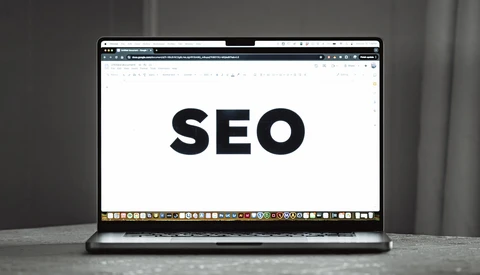 Laptop screen displaying the word 'SEO' in large black text on a white background.
