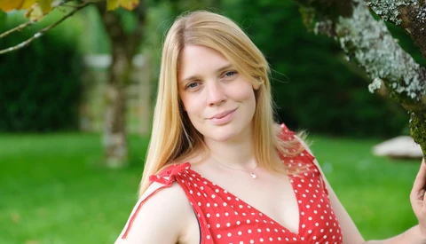 Young woman with blonde hair wearing a red polka dot dress in an outdoor garden setting.
