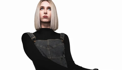 Woman with platinum blonde bob wearing black long-sleeve shirt and gray pinstriped vest over white background.
