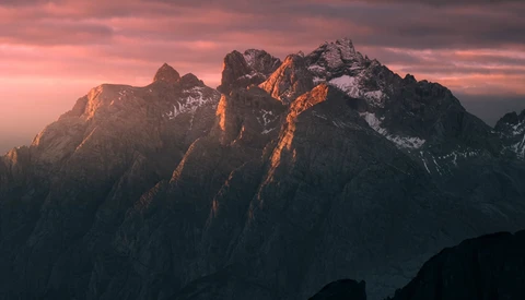 Jagged mountain peaks illuminated by golden alpenglow at sunset against a pink and purple sky.