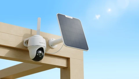 Solar-powered wireless security camera mounted on wooden beam with dual antenna and attached solar panel against blue sky.