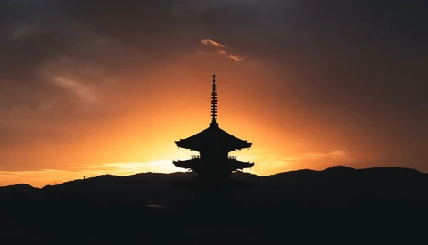 Silhouetted Asian pagoda backlit by a golden sunset sky with dramatic clouds.