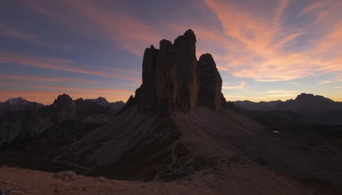Dramatic rocky mountain peaks silhouetted against a colorful twilight sky with golden and pink clouds.