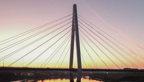 Cable-stayed bridge silhouetted against a dusky sky with golden and pink hues reflected in still water below.