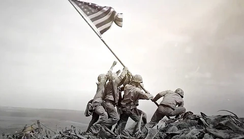 Soldiers raising an American flag on rocky terrain during overcast conditions.