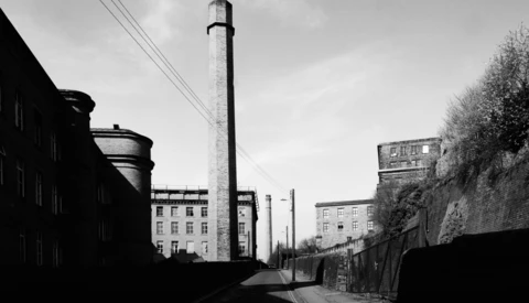 Industrial urban street with tall chimney and apartment buildings in black and white.