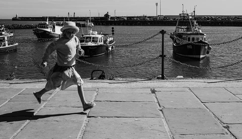 Runner in motion on a waterfront promenade with moored boats in the background.