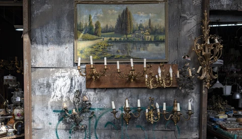 Weathered wall display with landscape painting, brass candelabras, and decorative sconces in vintage setting.