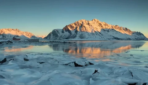 Snow-covered mountain reflected in partially frozen water at golden hour.