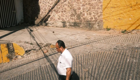 Man in white shirt standing in sunlit alley with geometric shadows and yellow wall.