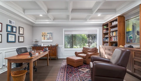 Home office with wood desk, leather seating, coffered ceiling, and built-in shelving.