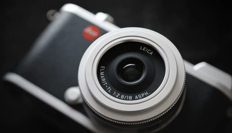 Leica Elmarit lens on mirrorless camera body against dark background.