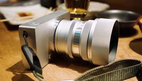 White mirrorless camera with silver telephoto lens on wooden table.
