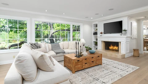 Modern living room with cream sectional sofa, wooden coffee table, and fireplace with mounted TV.