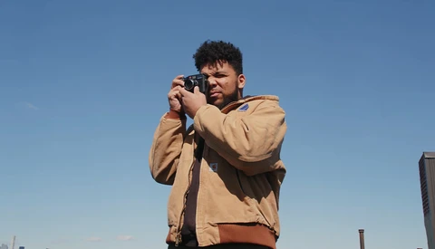 Photographer holding a camera up to his face while looking through the viewfinder against a clear blue sky.