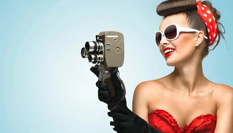 Woman in vintage-style outfit holding a film camera up to her face.
