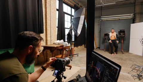 Photographer operating camera on tripod during studio shoot with model and lighting setup.
