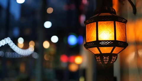 Ornate brass lantern with glowing amber glass panels hanging in an urban street at dusk.
