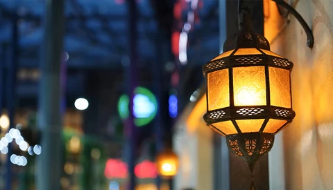 Ornate hanging lantern glowing warmly against an urban street at dusk, with blurred city lights in the background.