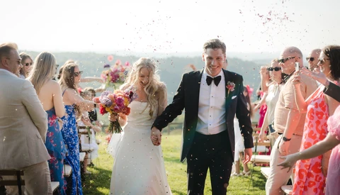 Newlyweds walk through a cheering crowd during outdoor ceremony recessional.
