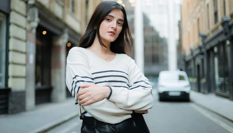 Young woman in striped sweater standing on urban street with classical architecture.