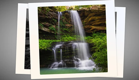 Multi-tiered waterfall cascading into an emerald pool surrounded by moss-covered rocks and lush green vegetation.