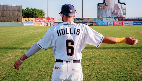 Baseball player wearing number 6 jersey standing on grass field with arms outstretched.