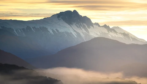 Layered mountain peaks bathed in golden sunrise light with misty valleys below.