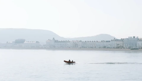 Small red boat on calm water with misty waterfront buildings in the background.
