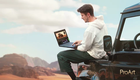Man sitting on truck tailgate editing photos on laptop with desert landscape in background.