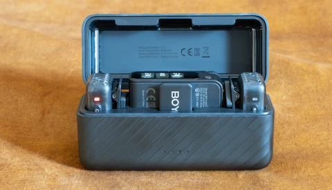 Open gray protective case containing a wireless microphone system with transmitter, receiver, and battery compartments on wooden surface.