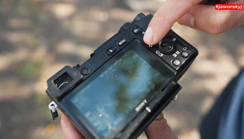 Hands holding a mirrorless camera displaying a blue-tinted live view on its rear LCD screen.