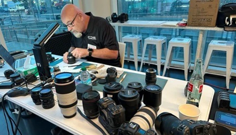 Photographer reviewing camera lenses and equipment at a desk in a high-rise office with city views.