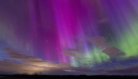 Aurora borealis display with vibrant magenta and green bands arcing across a twilight sky above a dark landscape.