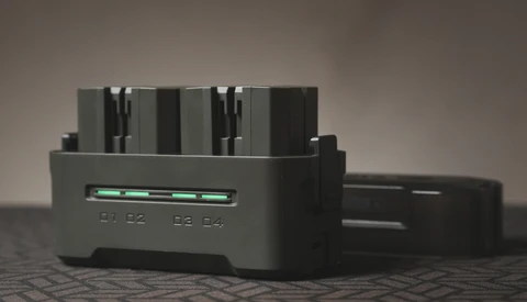 Black battery charger with four AA or AAA slots and a green LED indicator light on the front panel.
