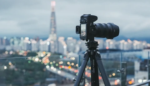 Professional camera on tripod mounted on elevated vantage point overlooking cityscape at dusk.