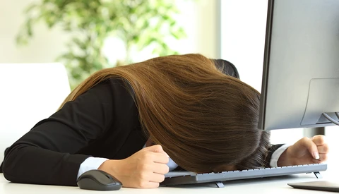 Person slumped over desk with head resting on keyboard, displaying exhaustion or burnout.