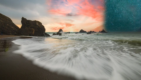 Long-exposure seascape with smooth waves rolling onto a sandy beach at sunset, rocky outcrops visible in the background.