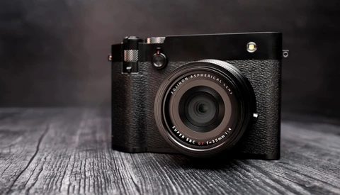 Black rangefinder camera with textured leather grip and fixed lens on wooden surface.