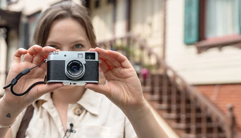 Woman holding a rangefinder film camera up to her face, positioned to take a photograph.