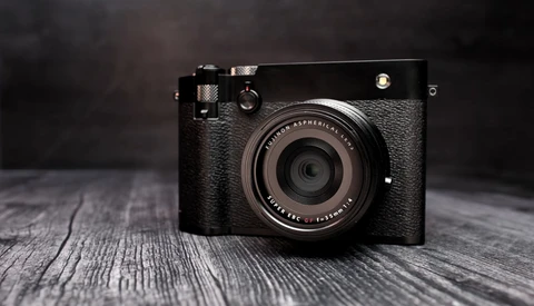 Black rangefinder camera with textured leather body on weathered wooden surface.