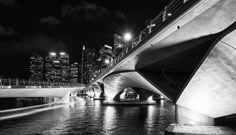 Modern bridge underpass with curved concrete architecture and illuminated city skyline at night.
