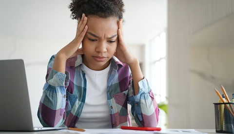 Person holding head with hands while looking down at laptop, showing signs of stress or concentration.