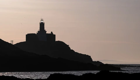 Lighthouse silhouetted against a twilight sky on a rocky coastal promontory.