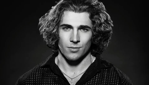 Black and white portrait of a man with shoulder-length curly hair and a chain necklace.