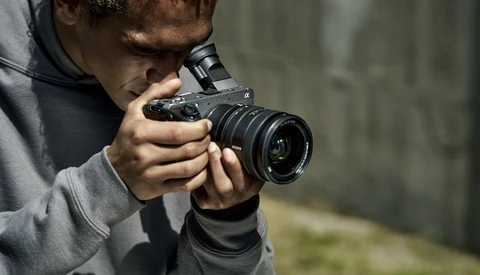 Young photographer holding a DSLR camera with telephoto lens while composing a shot outdoors.