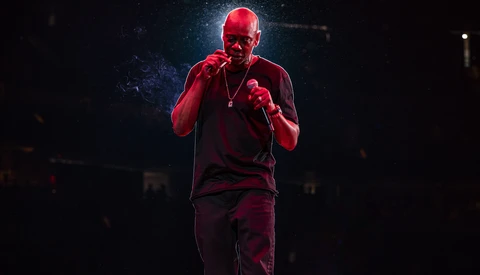 Performer on stage bathed in red lighting, holding a microphone with both hands.