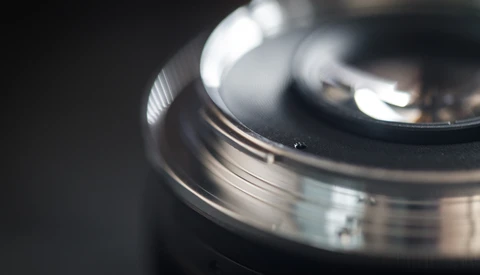 Close-up of a camera lens with selective focus, showing metal barrel and glass elements with shallow depth of field.