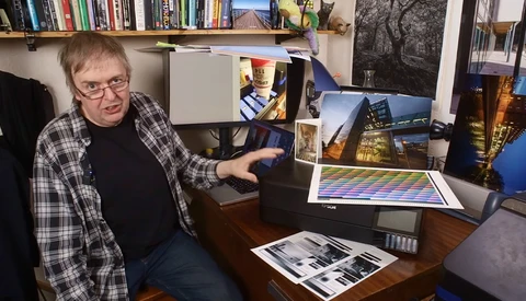 Photographer reviewing color-graded prints and digital displays at a desk workspace.