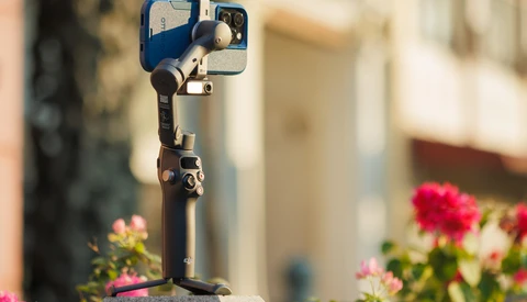 Smartphone mounted on a gimbal stabilizer with pink flowers in soft focus background.
